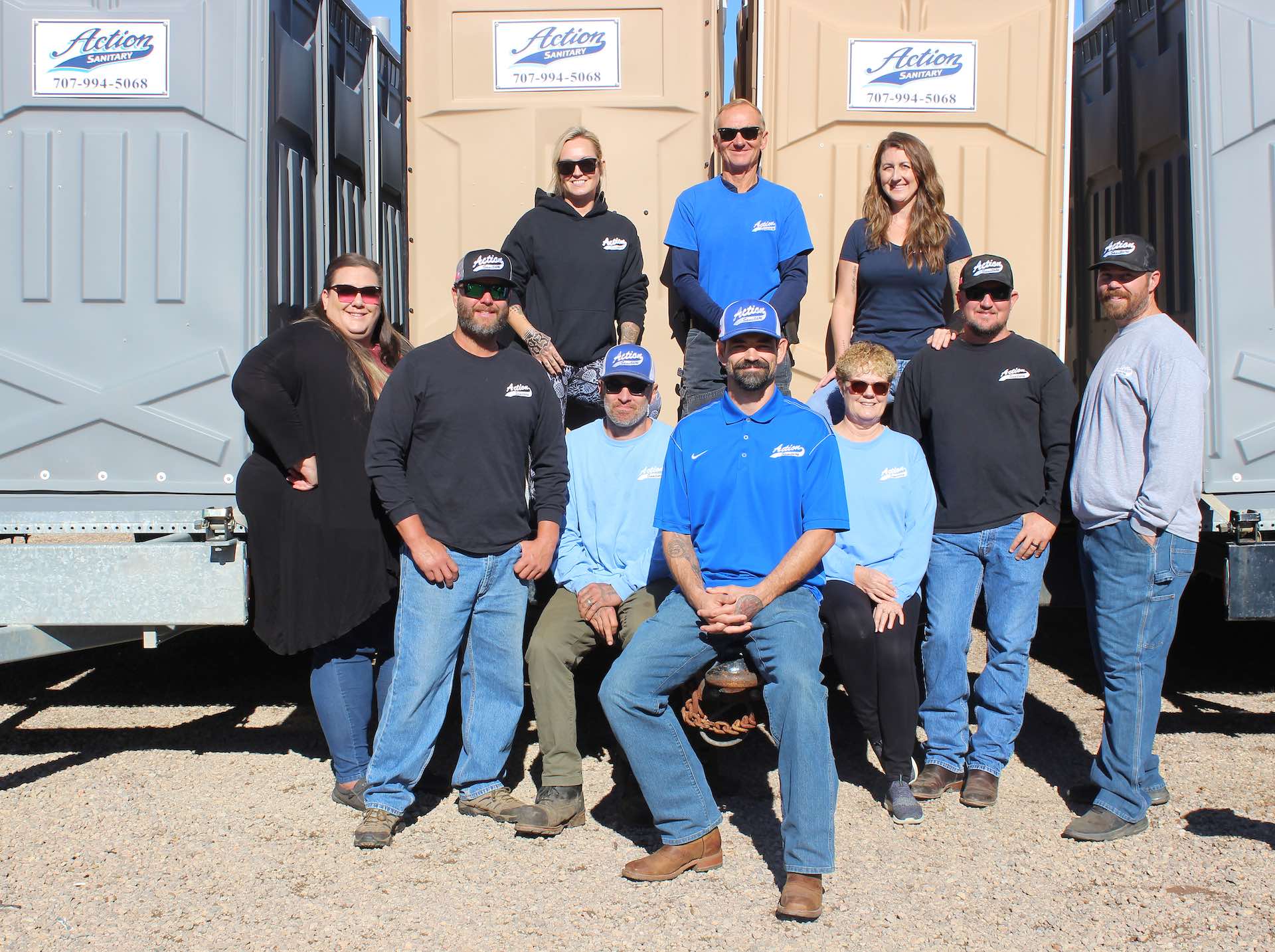 Action Sanitary company picture with owners and main employees leaning against porta potties